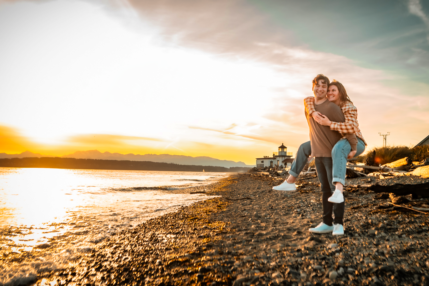 Couple embraces on rocky beach at sunset with golden light reflecting off calm waters.