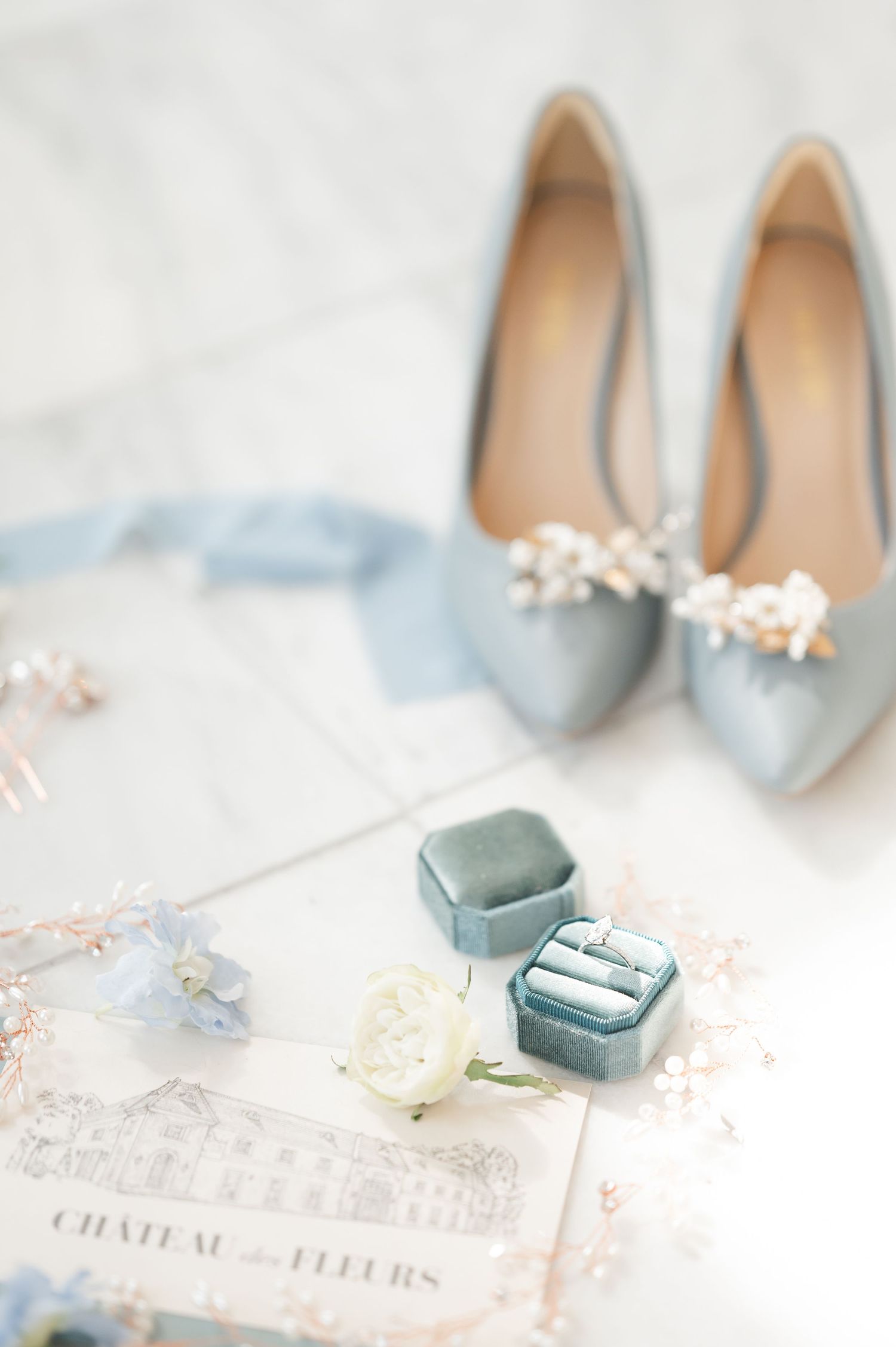 Pale blue wedding shoes and vintage decor with ring boxes on an elegant invitation.