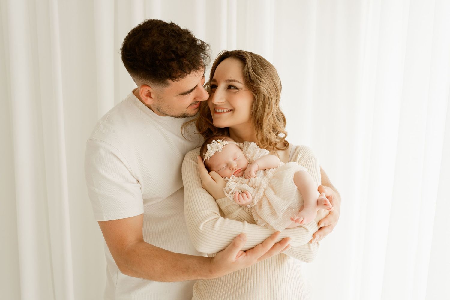 Tender family moment with parents and sleeping newborn baby in soft natural lighting.