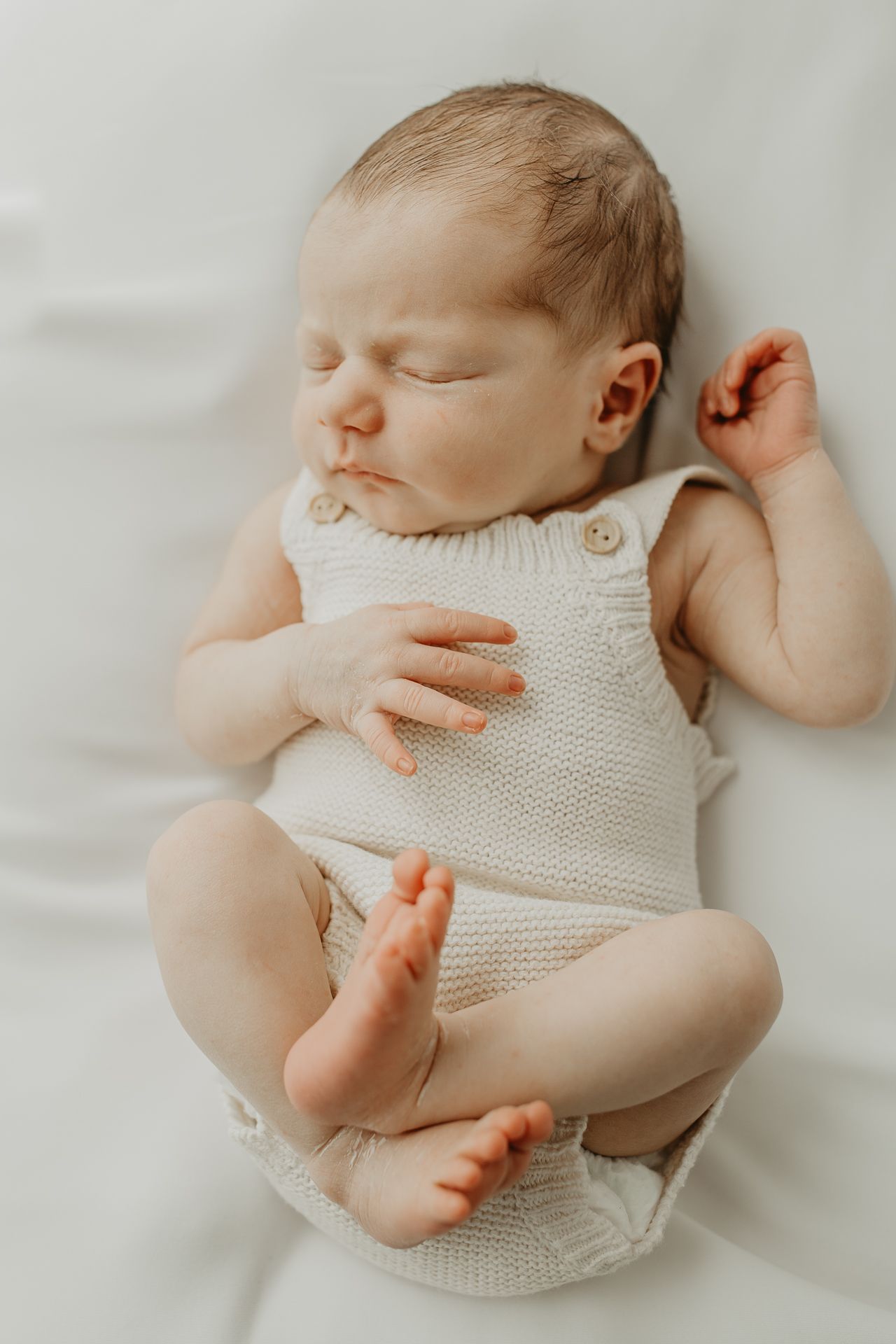 Sleeping newborn baby wearing white knit romper lying on soft white bedding in three various peaceful poses.