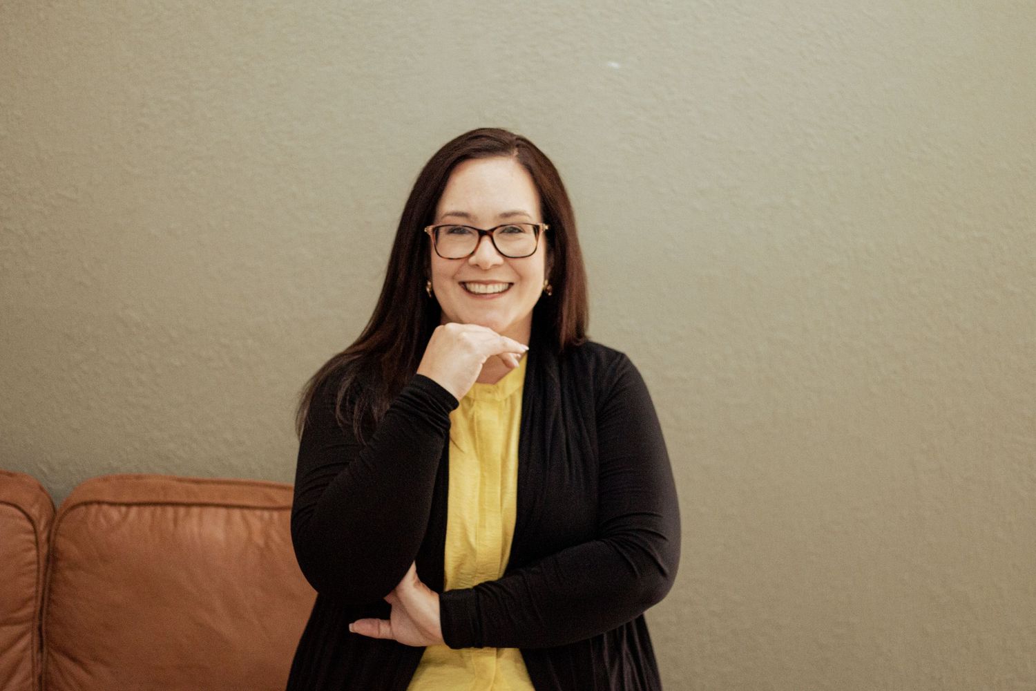 Professional woman in yellow top sits in front of neutral wall demonstrating varied expressions and poses.