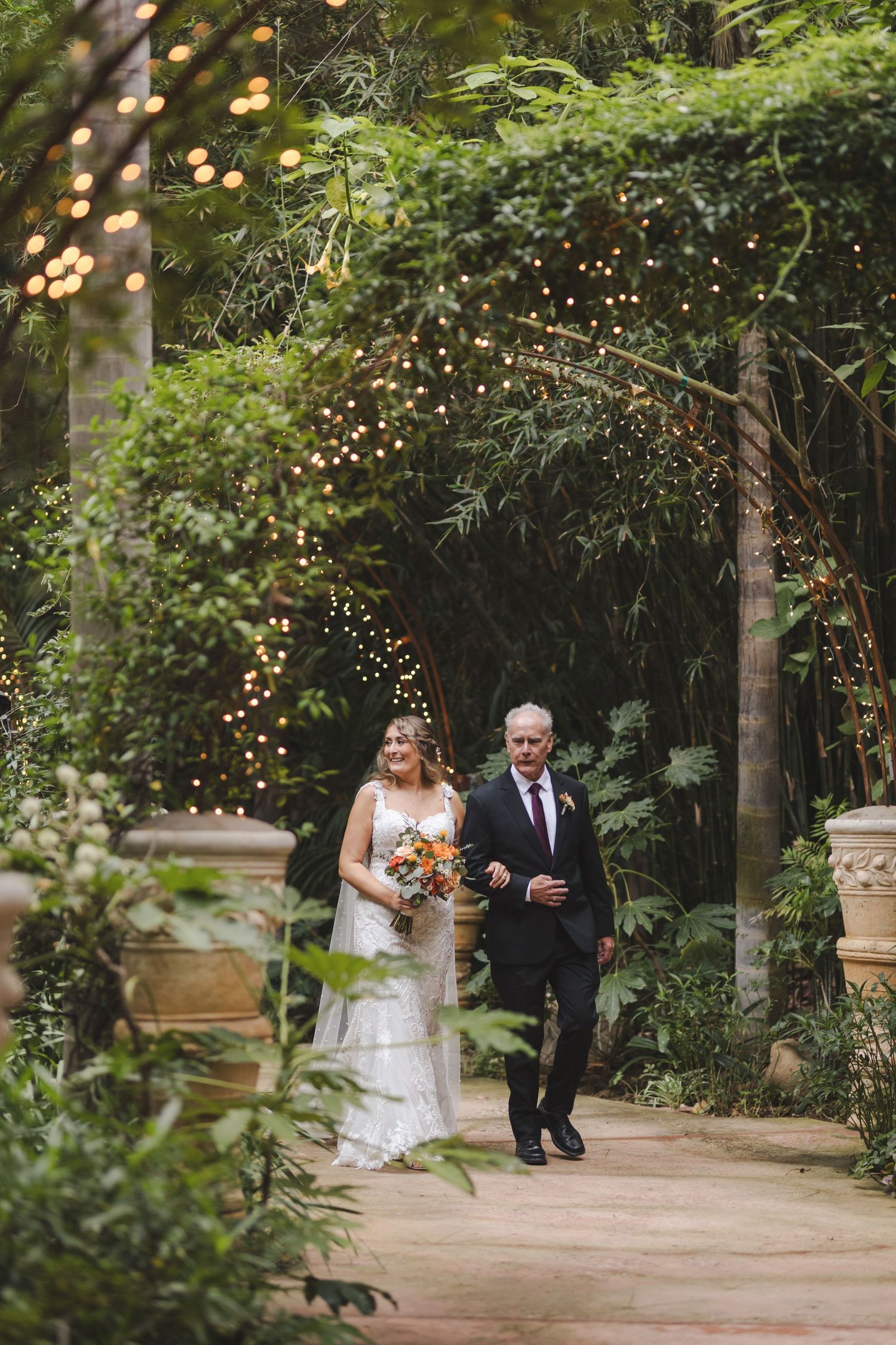 A wedding scene along a garden path with twinkling lights and lush greenery creating a magical atmosphere.