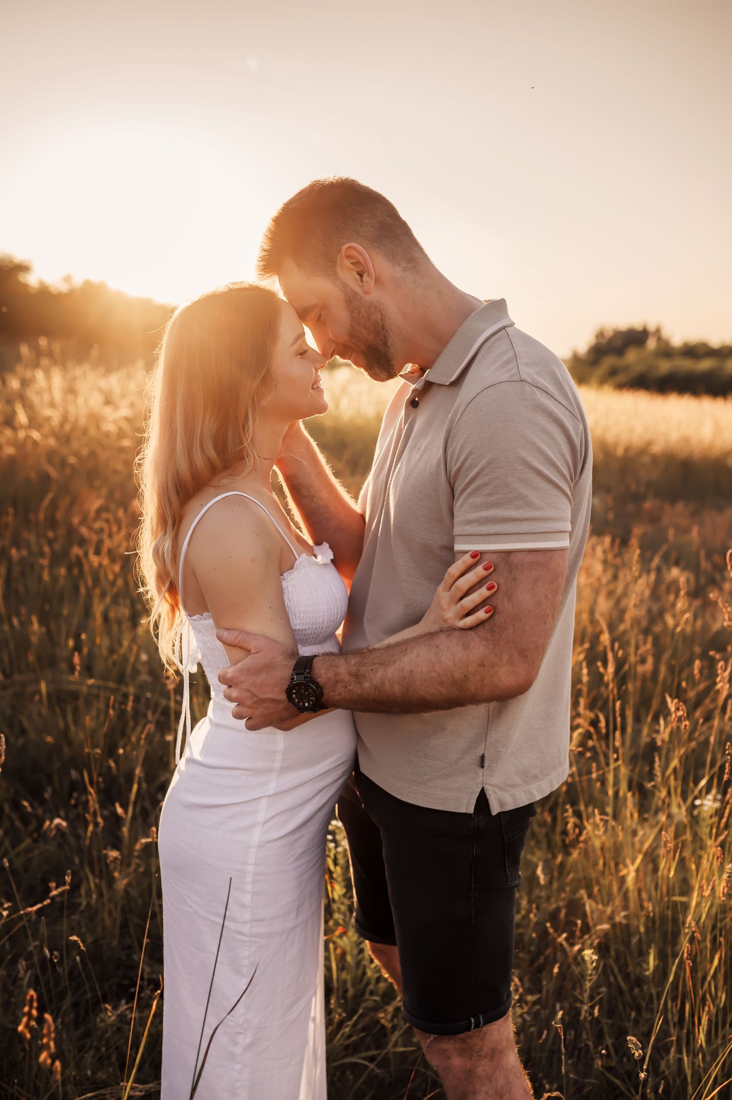 Romantic couple embrace in golden sunlit field at sunset as sunlight creates warm backlit glow through tall grass.