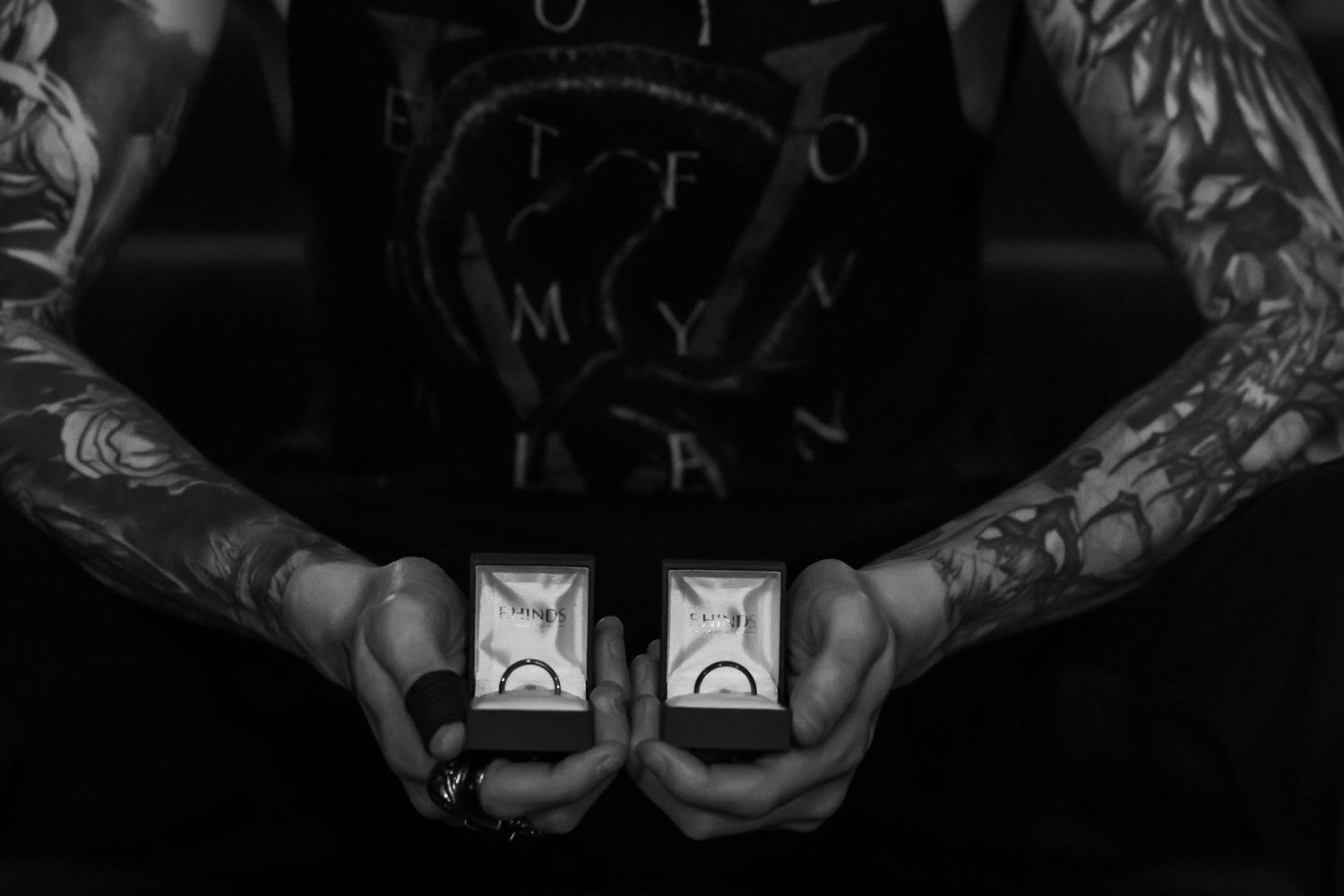Close-up shot of tattooed hands against a dark dramatic background.