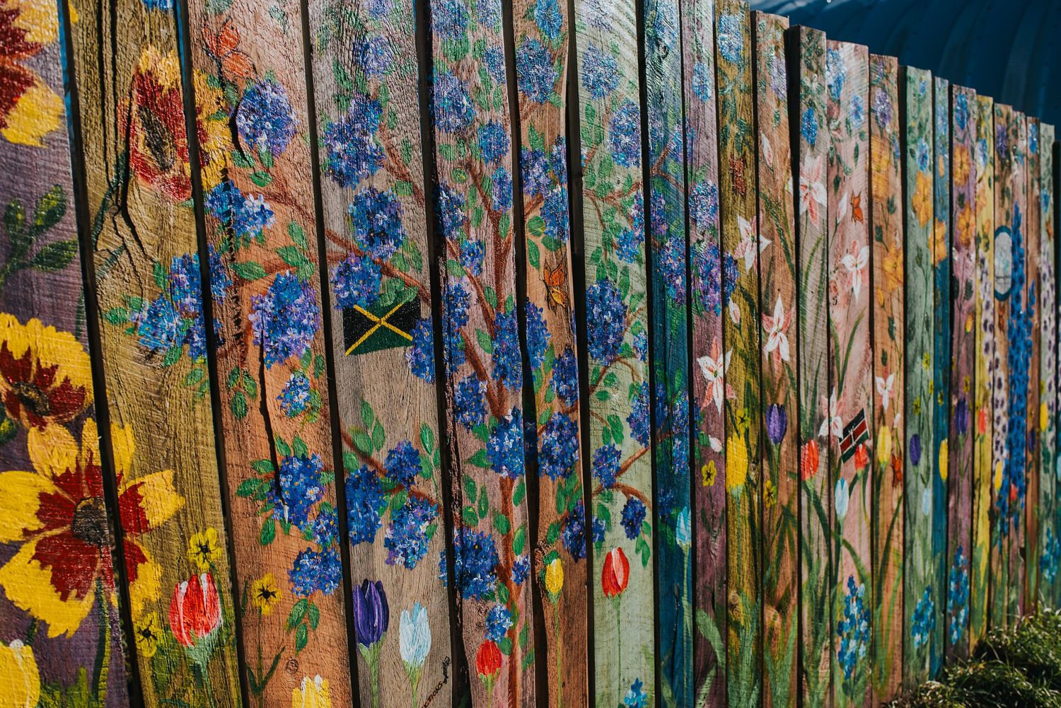 Colorful wildflowers and autumn leaves painted on wooden fence boards create a vibrant garden-themed outdoor mural.