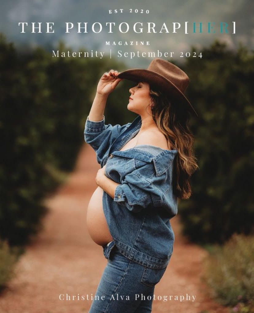 A maternity photo of woman in denim against nature backdrop wearing a wide-brimmed hat.