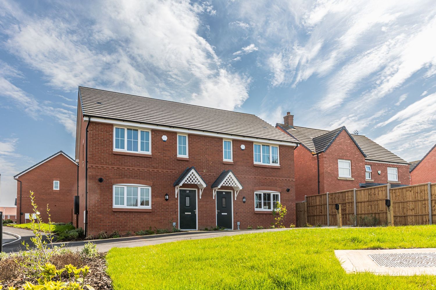 Modern red brick semi-detached house with well-maintained front lawn under dramatic cloudy sky.