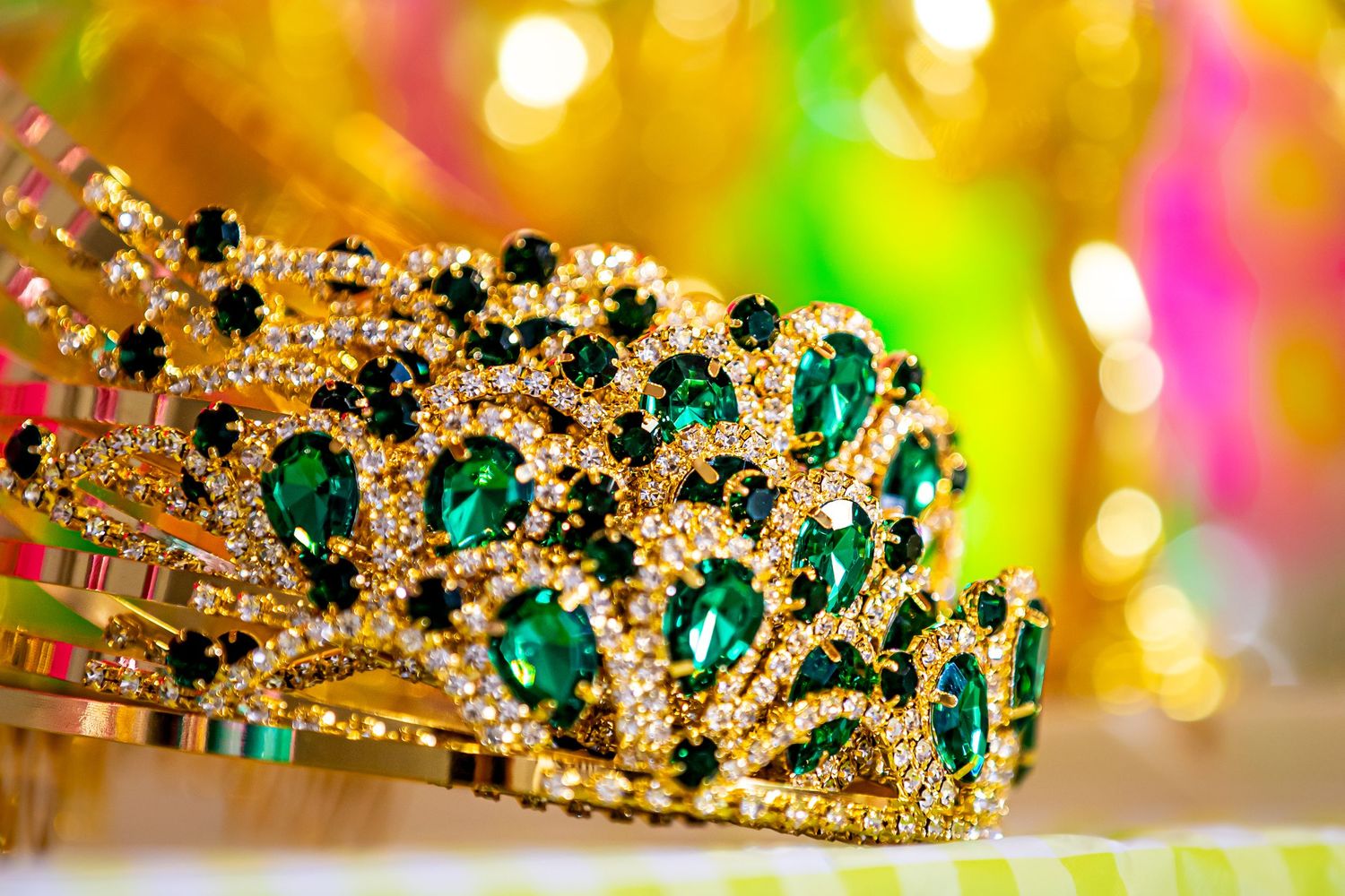Ornate gold and emerald crown with intricate details against colorful bokeh background.