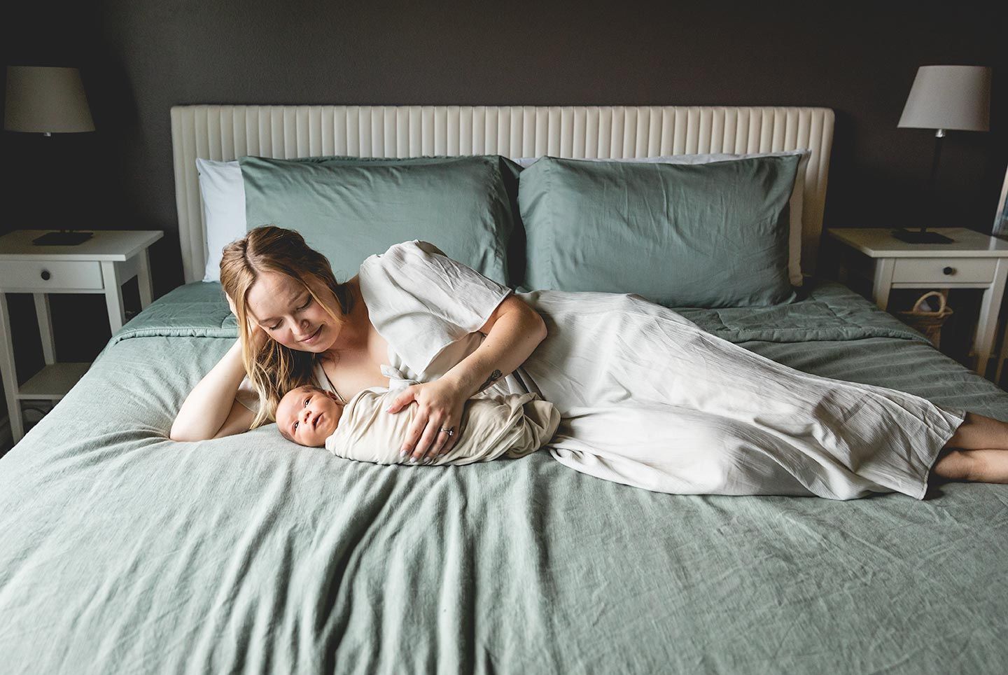 new mother laying next to her newborn baby on her bed