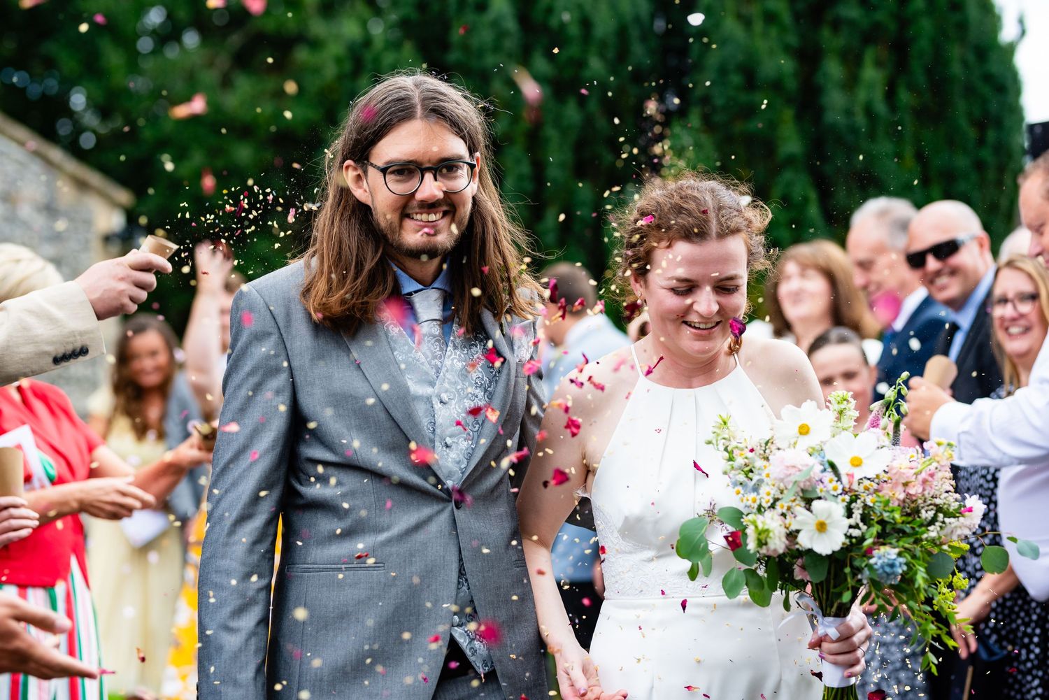 Joyful wedding moment with guests throwing confetti over the newlyweds outdoors.