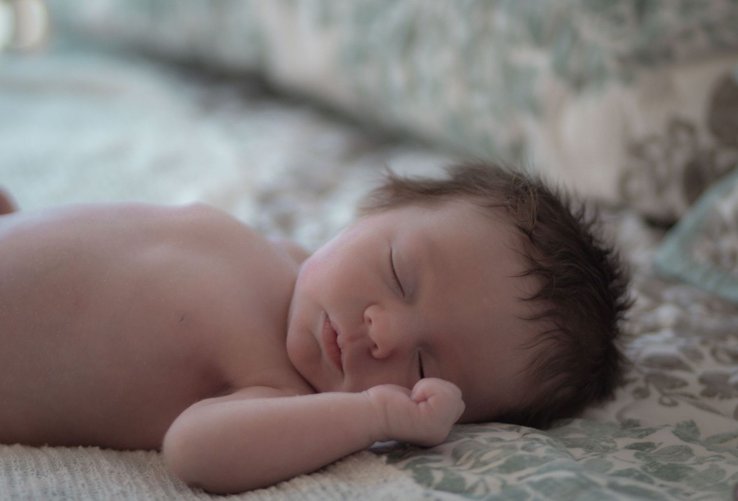Peaceful newborn baby with dark hair sleeping soundly on a soft floral blanket in a serene setting.
