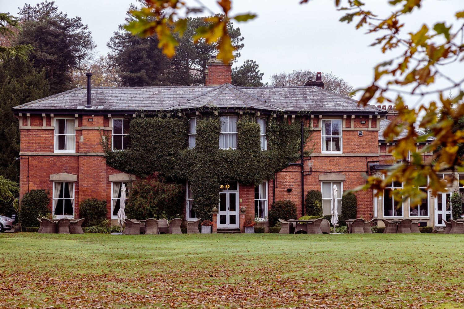 Large red brick manor house with symmetrical windows and landscaped grounds in autumn.