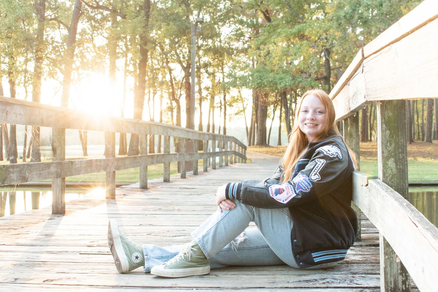 Portrait of someone in casual wear sitting on a wooden boardwalk at sunset in a forest setting.