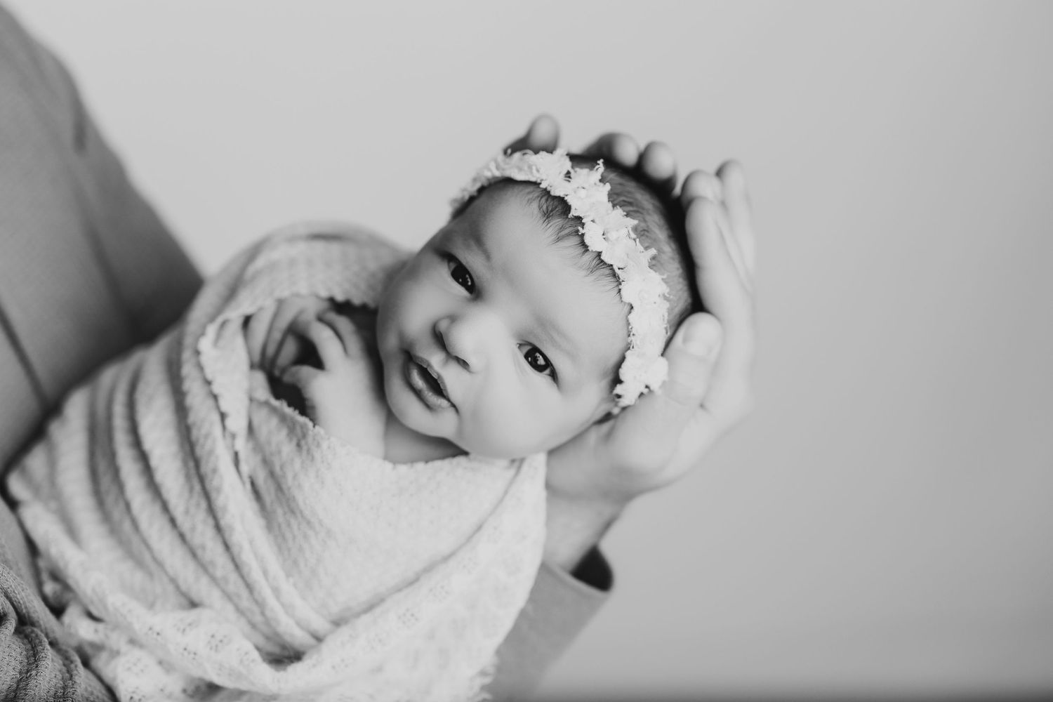 Black and white portrait of swaddled newborn with delicate headband.