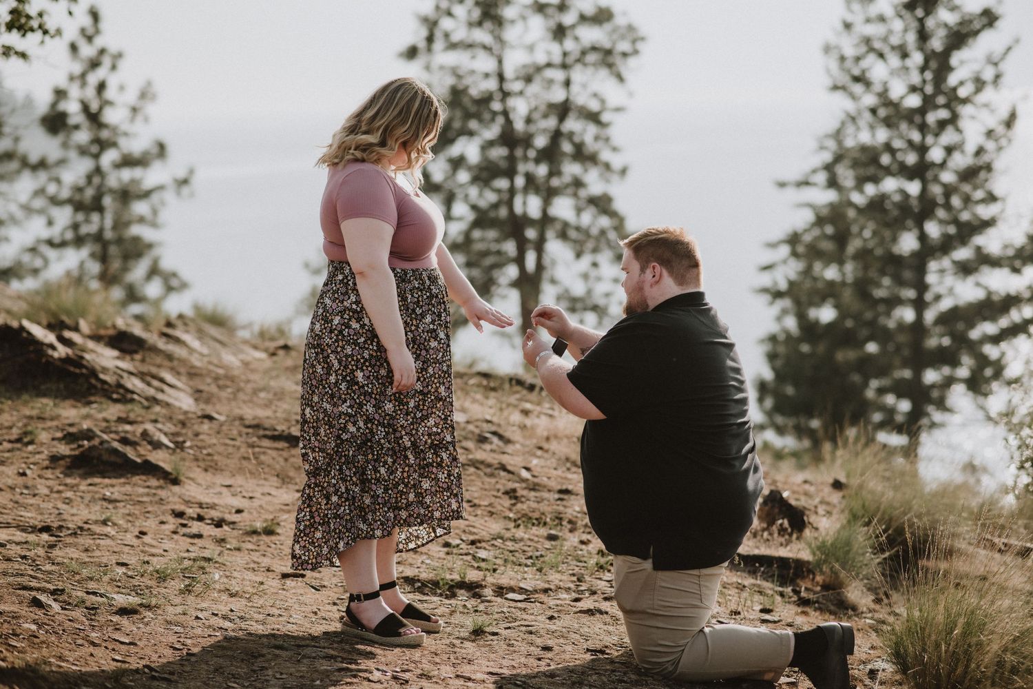 Couple photo for a surprise engagement shoot. Man down on one knee putting a ring on his fiance's  finger.