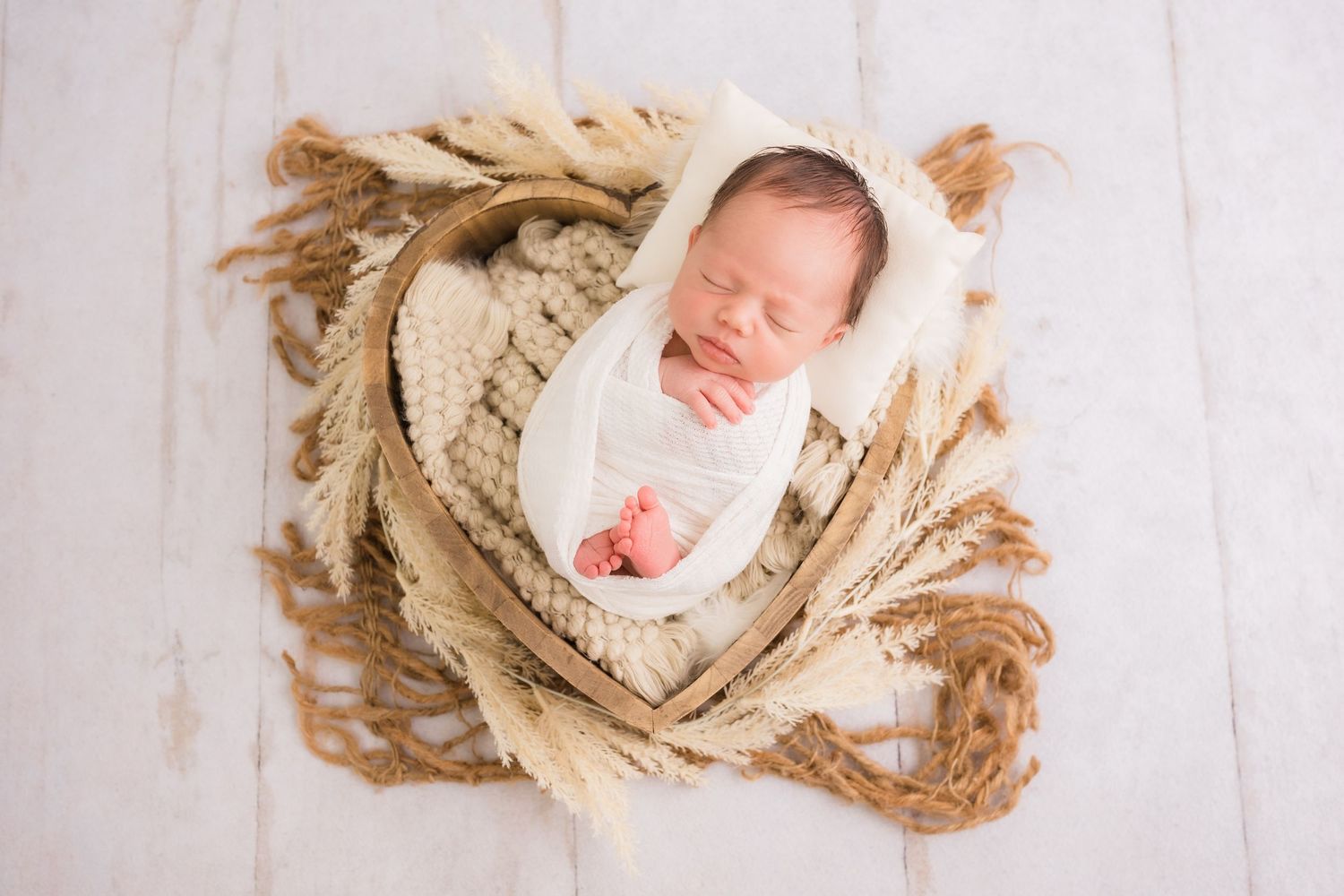 Peacefully sleeping swaddled newborn in cream wrap nestled in rustic basket with wheat.