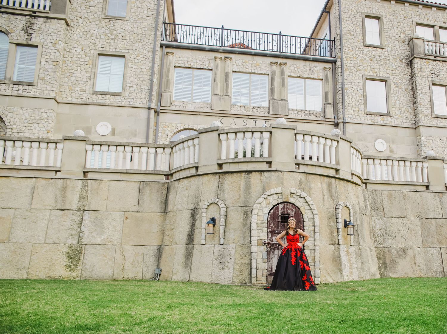 A stone castle exterior with balustrades extends across a green lawn under cloudy skies.