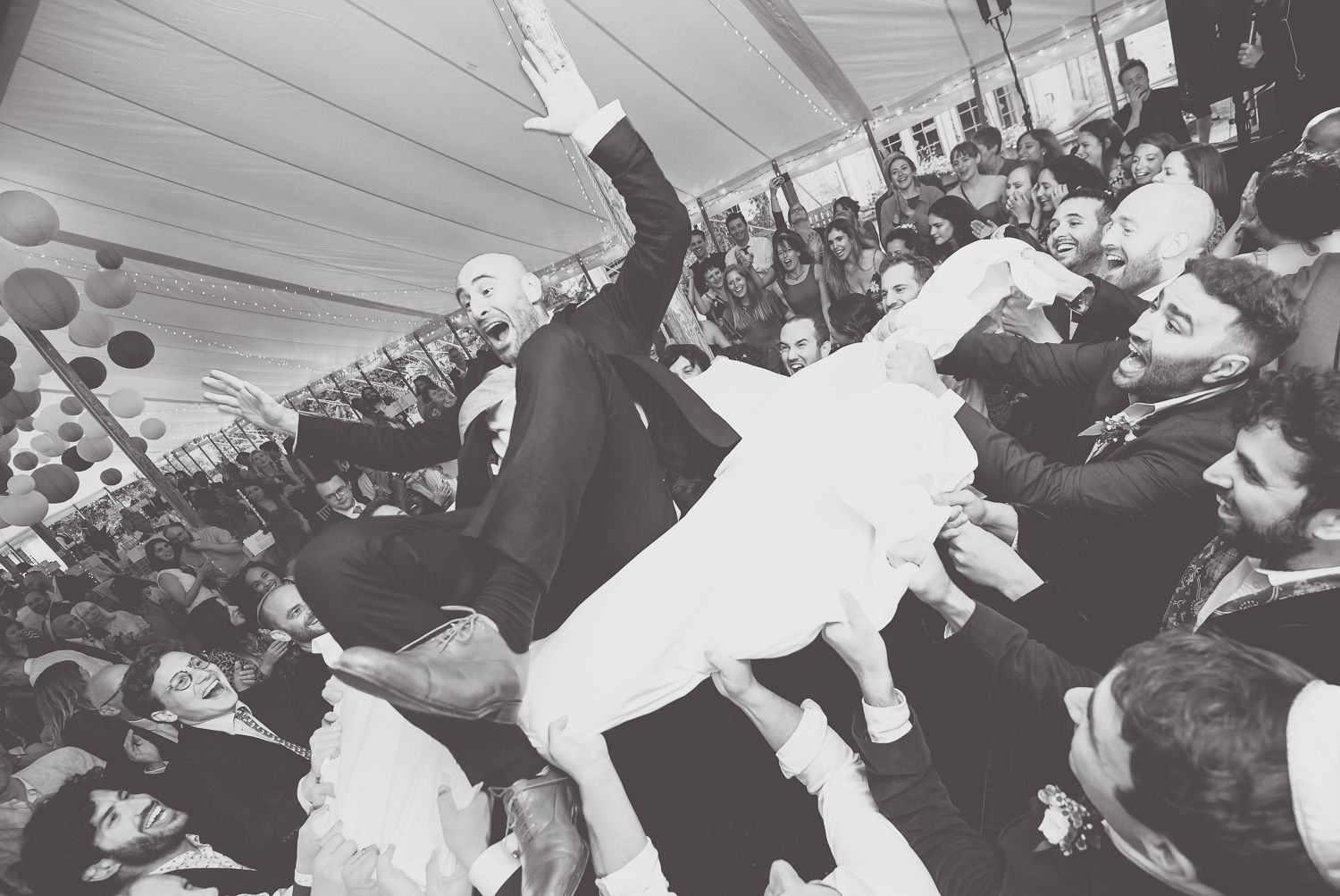 A vintage black and white photo shows celebratory crowd surfing at a lively event.