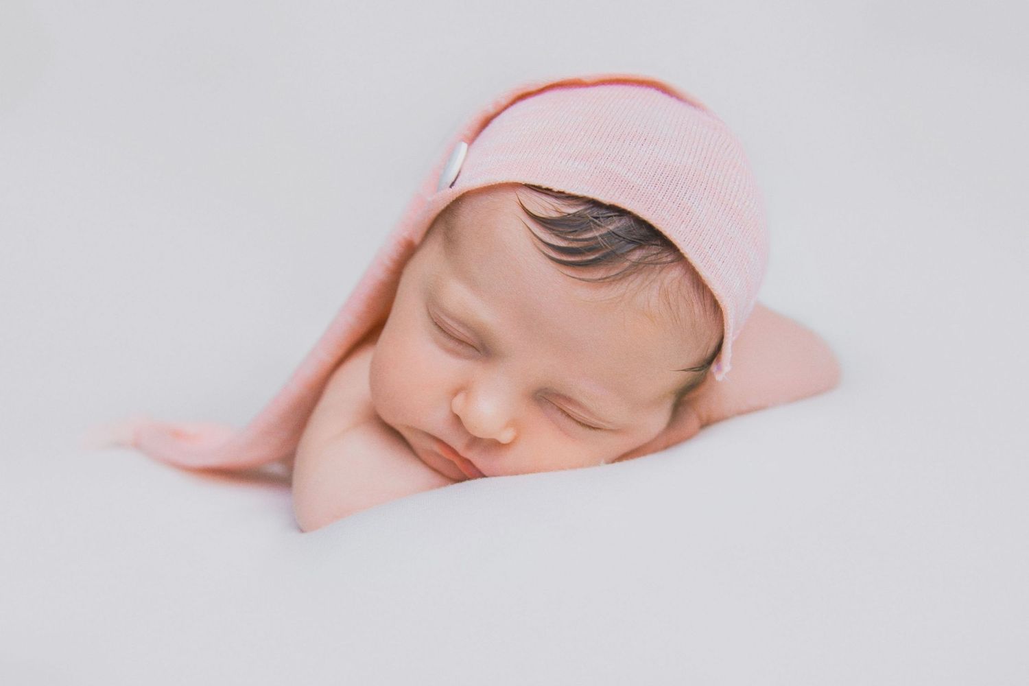 Sleeping newborn baby wrapped in soft pink blanket against light background.
