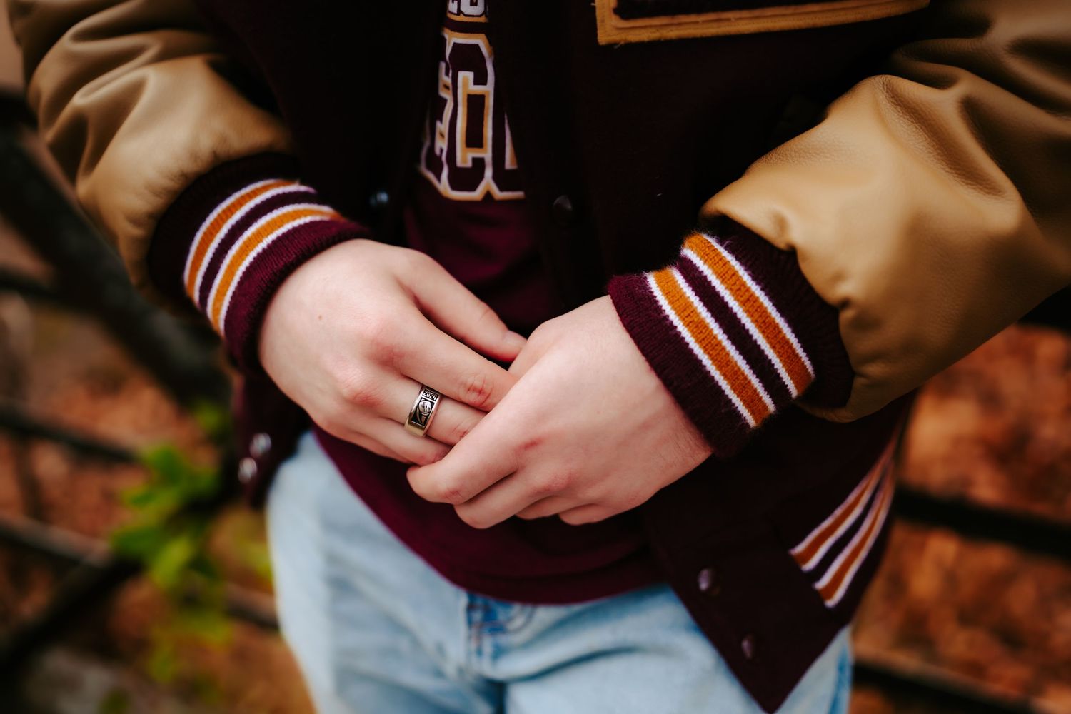 Close up of hands wearing varsity jacket with striped cuffs and a ring.