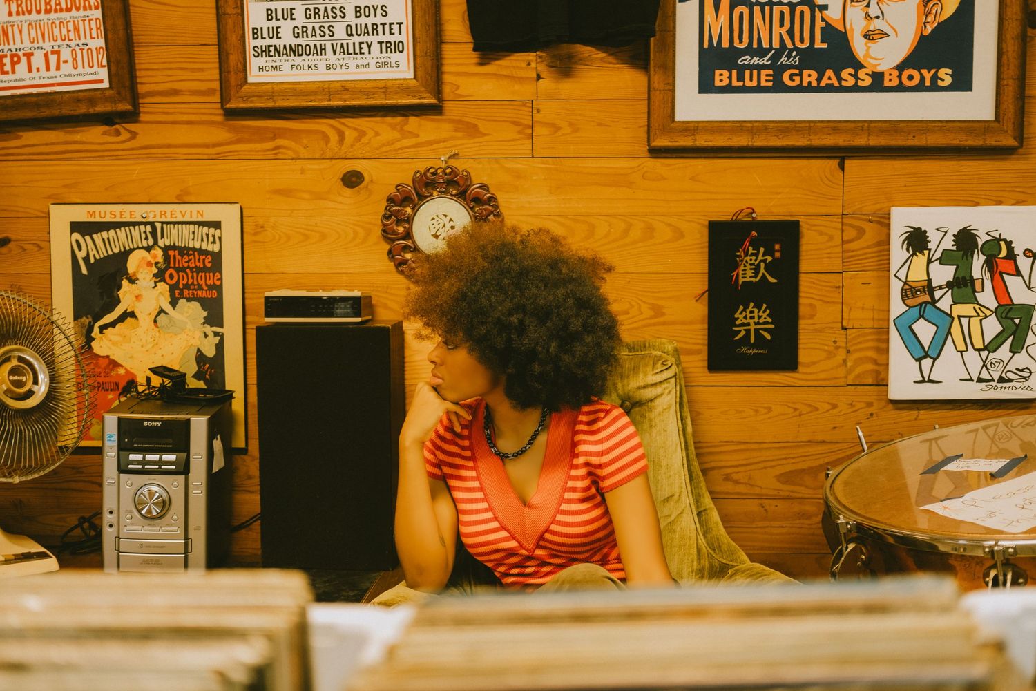 African American female seated in a light green chair surrounded by various framed images and artwork. Senior portrait