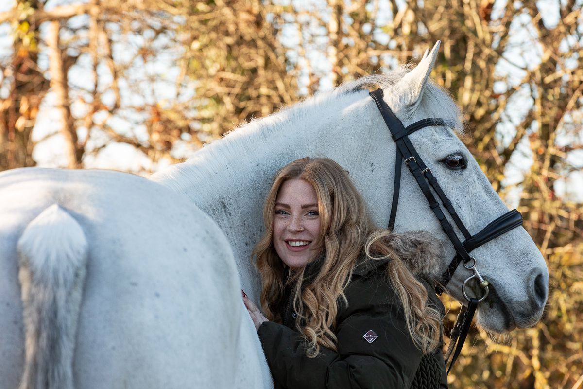 A beautiful white horse stands close while someone in black clothing poses with them.