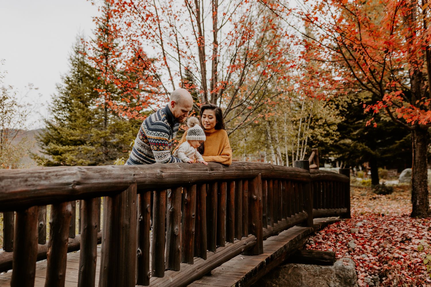 Couple sharing an intimate moment on a wooden bridge surrounded by autumn foliage.