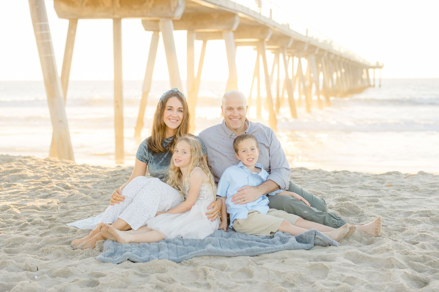 People relaxing on a sandy beach at sunset with golden light filtering through pier pillars.