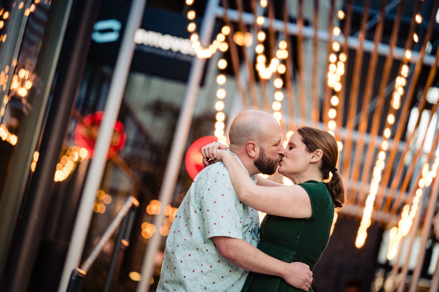 A romantic moment under string lights as a couple shares an intimate kiss outside.
