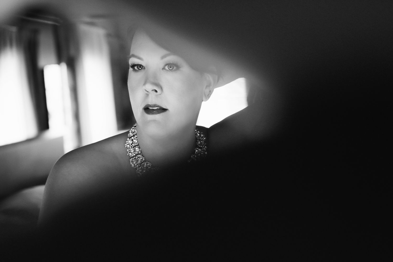 Dramatic black and white portrait with jewelry in moody car lighting.