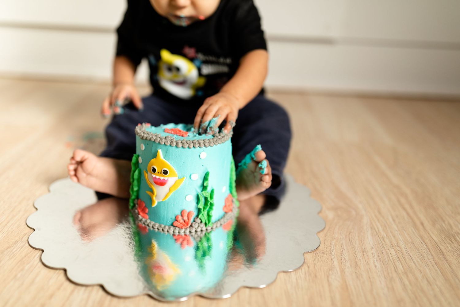 Small child playing with a teal decorative container on a wooden floor.
