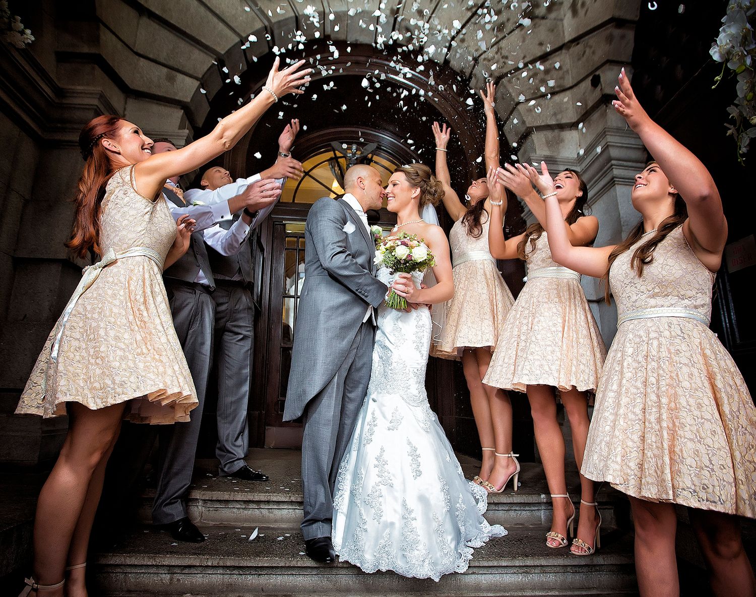 Bridal party celebrates with confetti toss on stone steps.