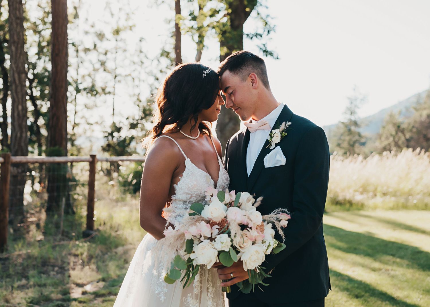 A couple shares an intimate moment during their outdoor wedding ceremony while holding a delicate blush and white bouquet.