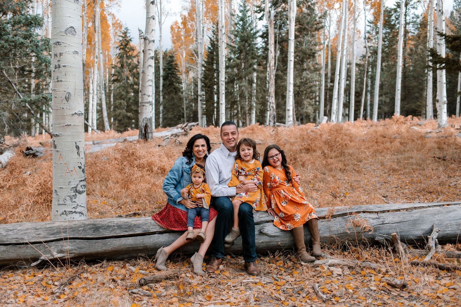 Family sits together among tall aspen trees with autumn colors in the forest.