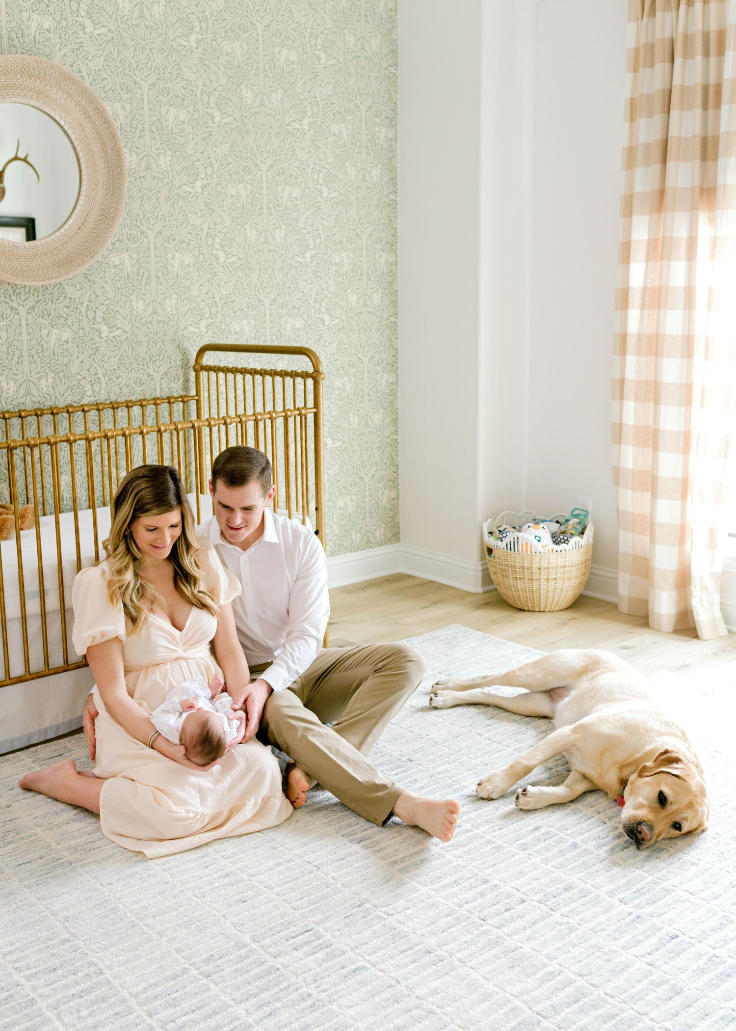 mom and dad sitting in front of crib, holding and admiring newborn son. family dog lays to the side of them.