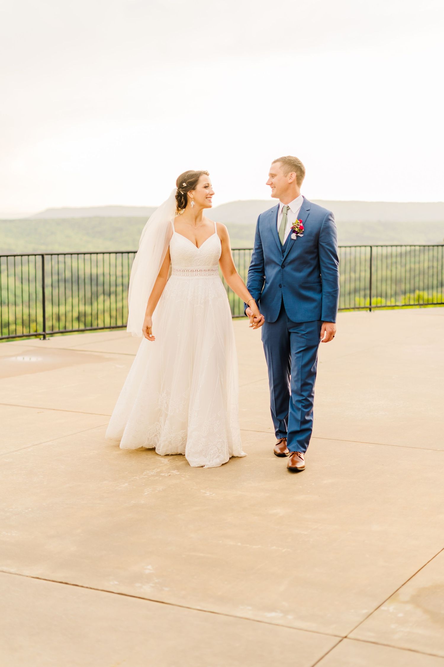 Newlyweds walking together on terrace overlooking mountain vista.
