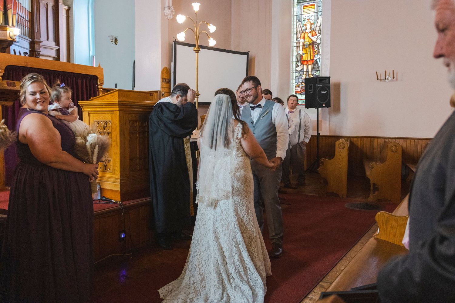 Wedding ceremony taking place inside a traditional church with stained glass windows.