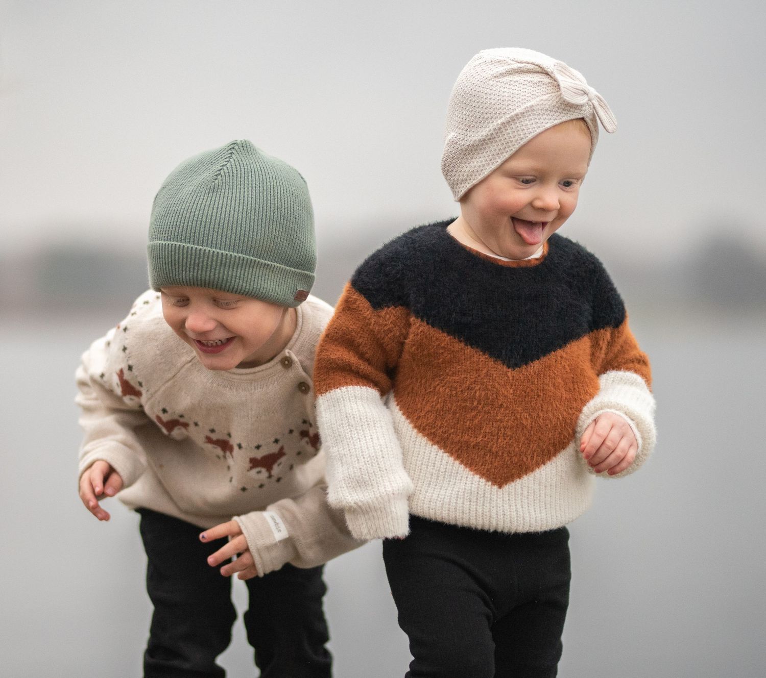 Two small children in winter clothing running and laughing together.