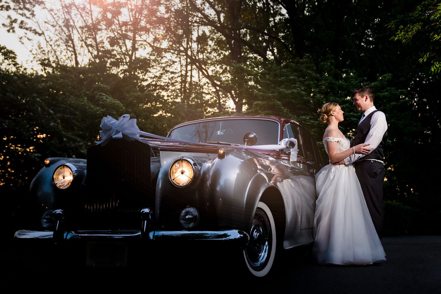 Classic vintage car serves as an elegant backdrop for wedding portraits at sunset.