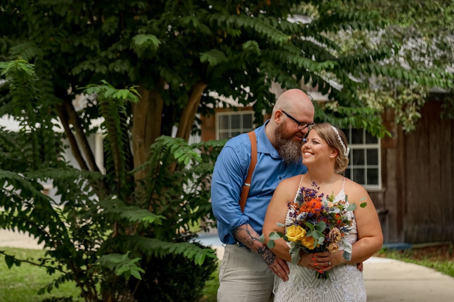 A couple shares an intimate moment in a lush garden setting with colorful wildflower bouquet.