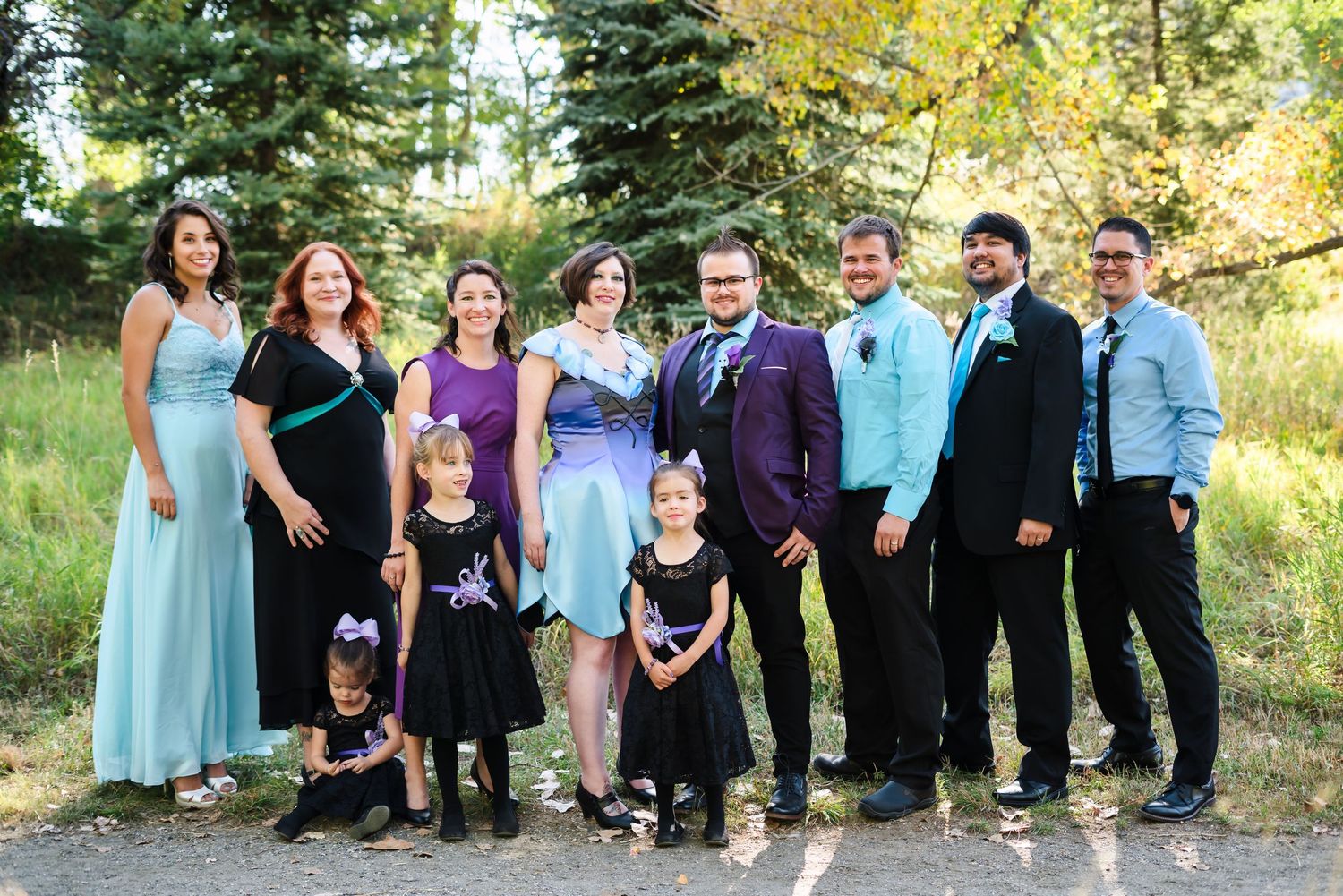 A wedding party poses together outdoors in formal attire with blue and purple color scheme.