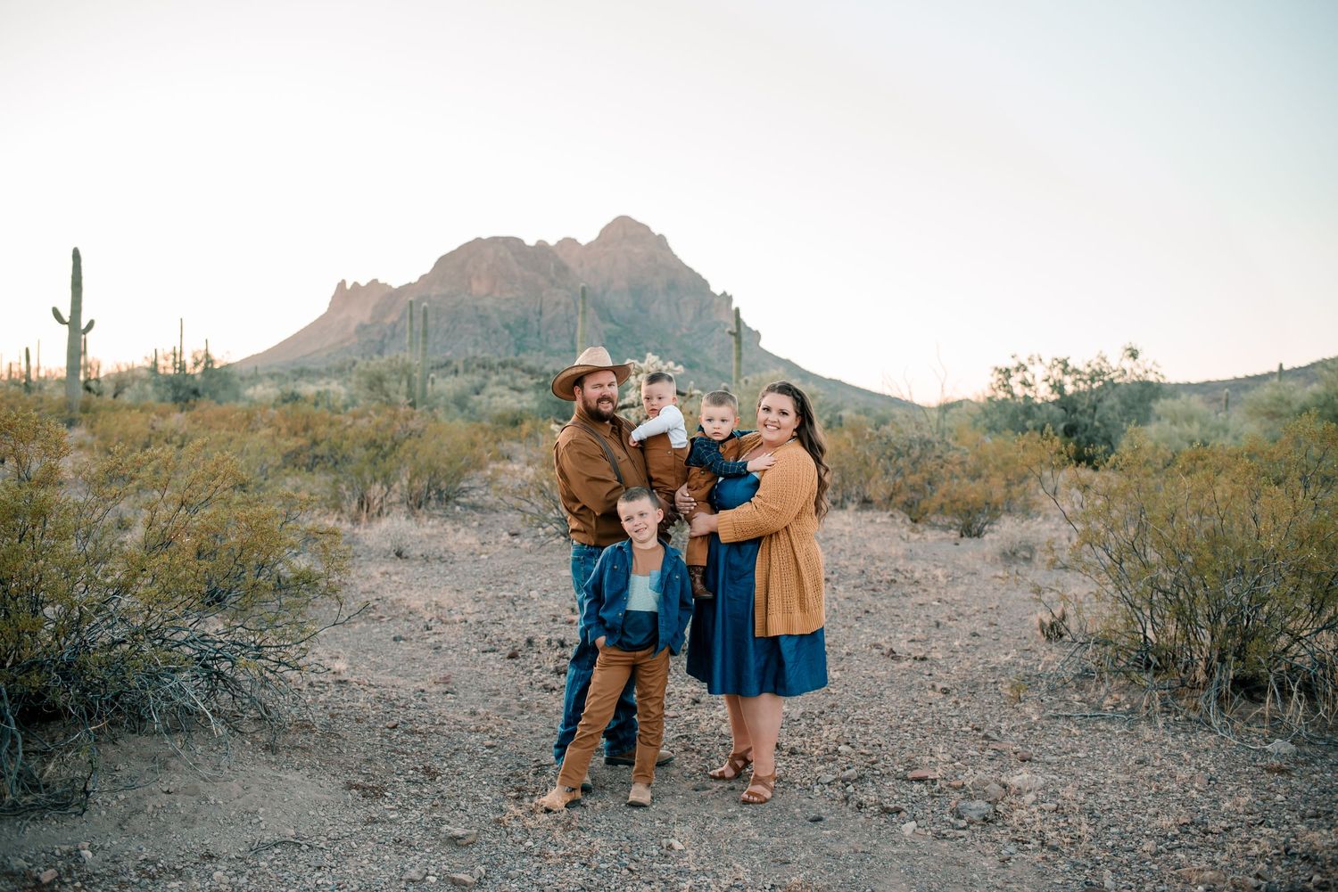 A family poses together in a desert landscape with mountains and cacti in the background.