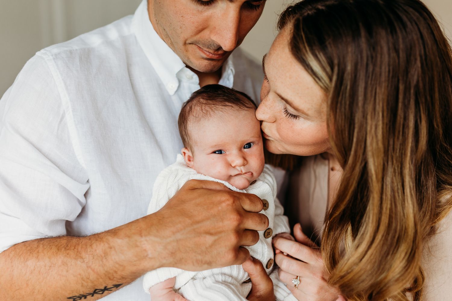 mother in Anthropologie dress kissing newborn baby with father