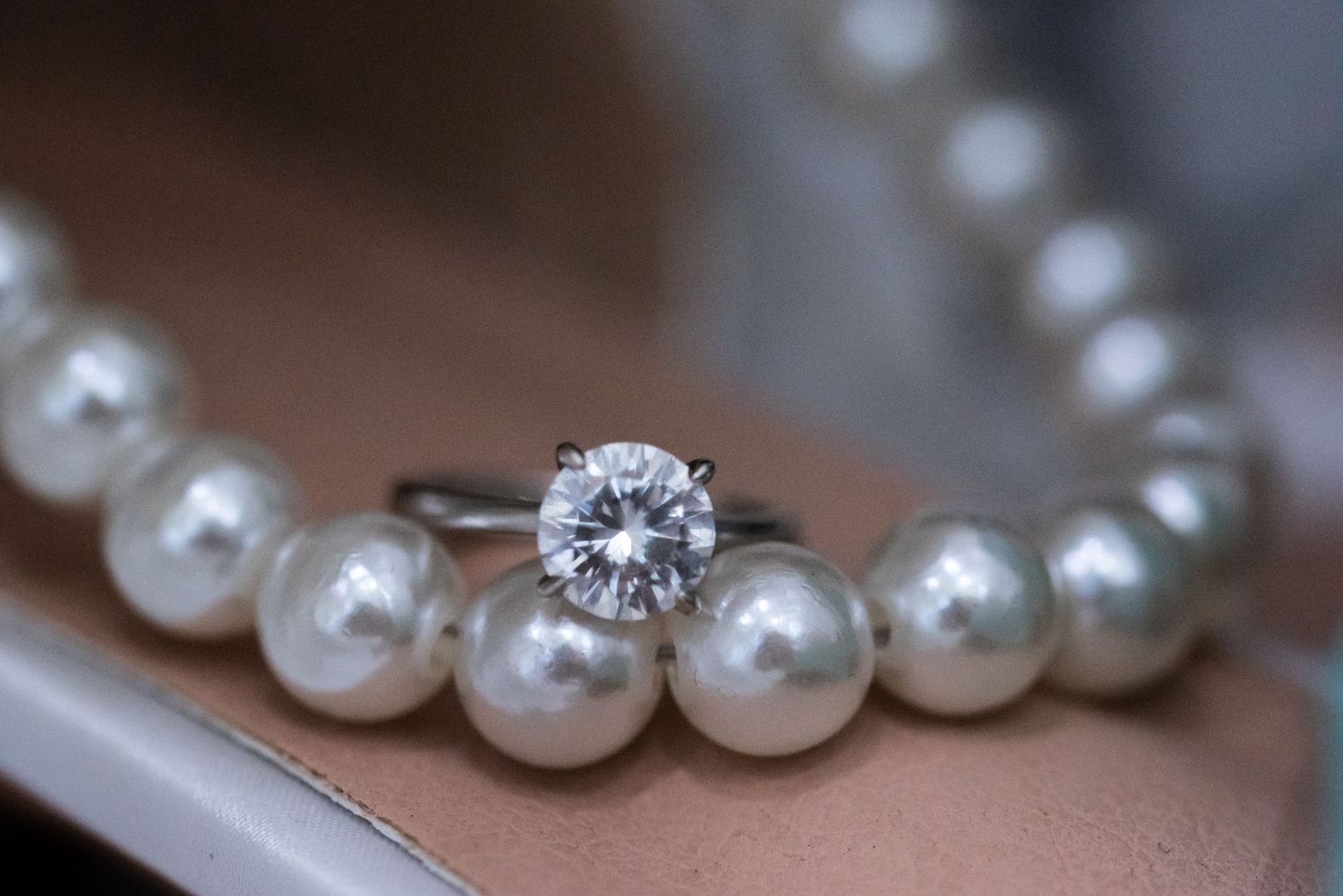 Closeup of pearl necklace with diamond ring detail.