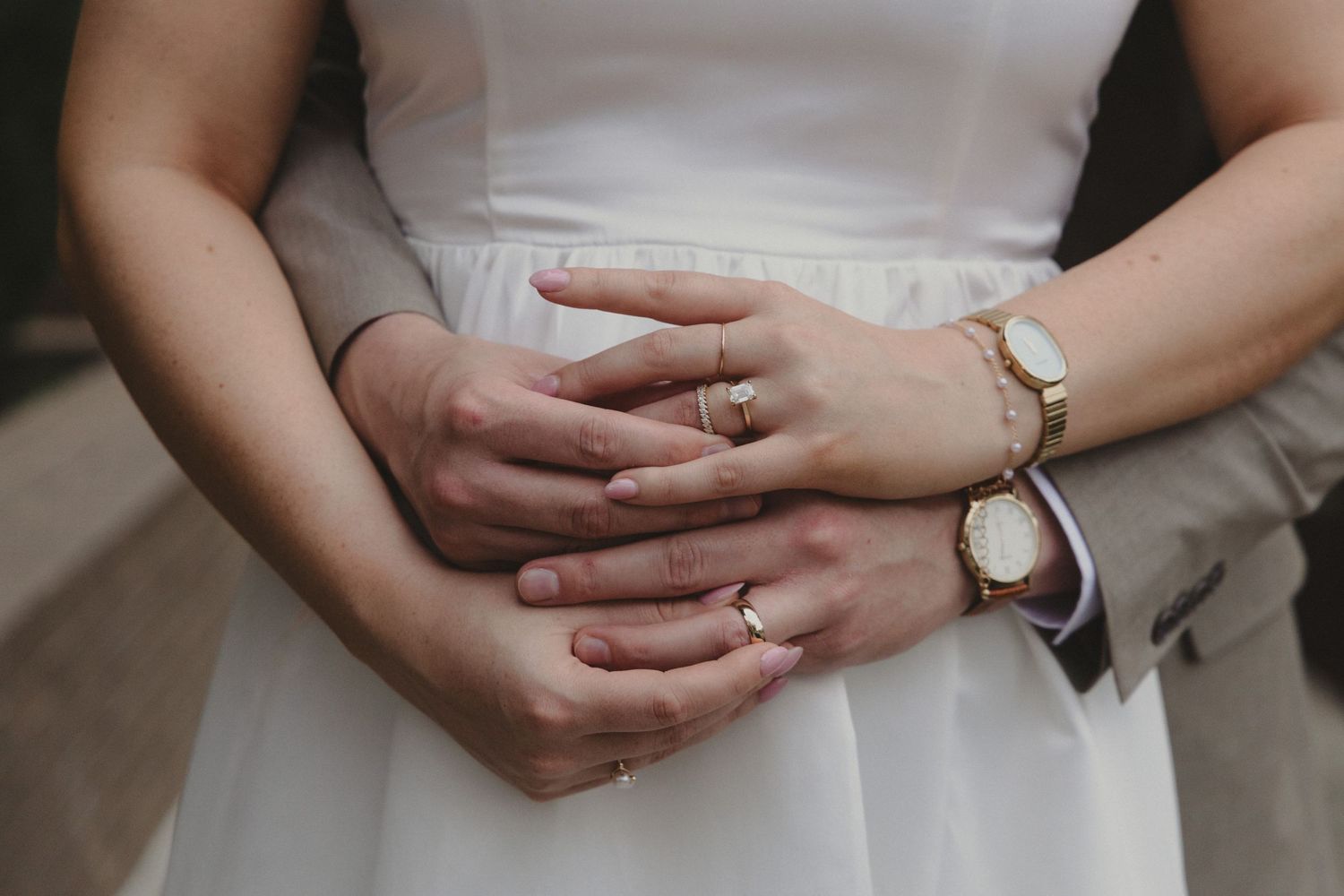 Close-up of hands wearing rings and a wristwatch against a white dress.