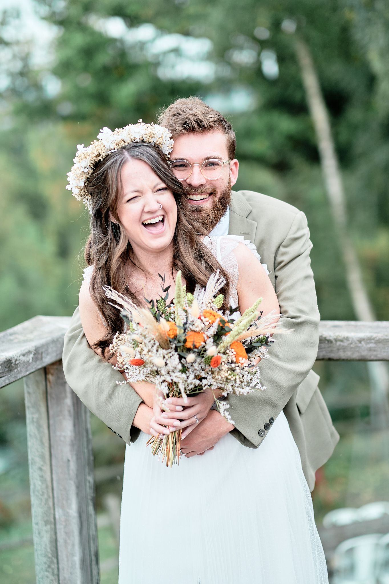 A joyful wedding moment captured on a rustic wooden bridge with a colorful wildflower bouquet.