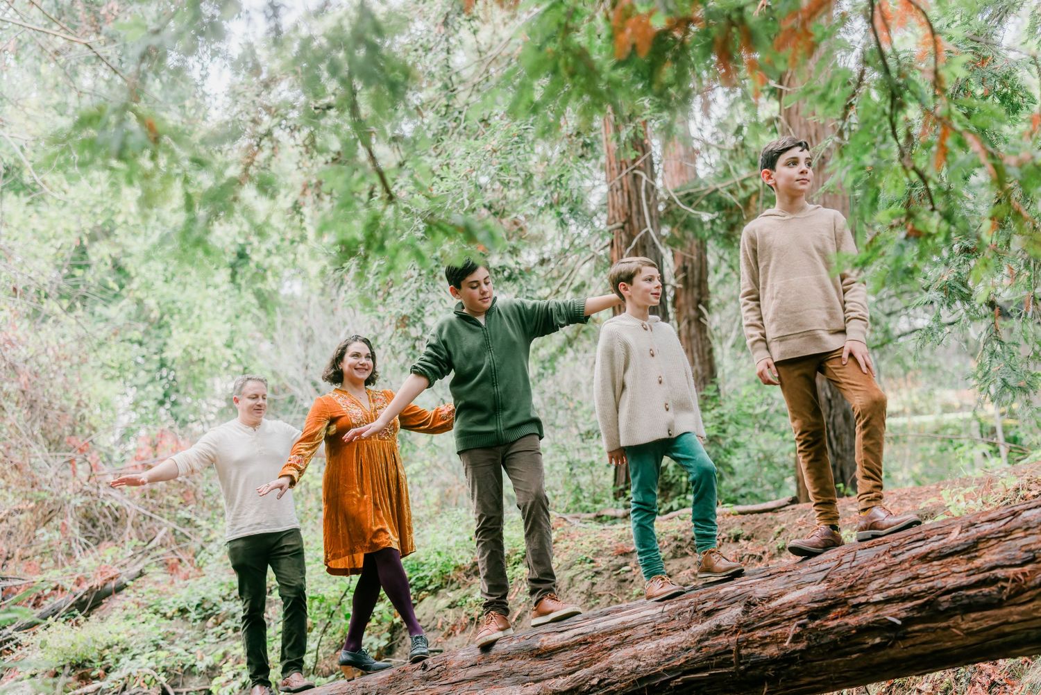 Group balancing together on fallen log in autumn forest setting.