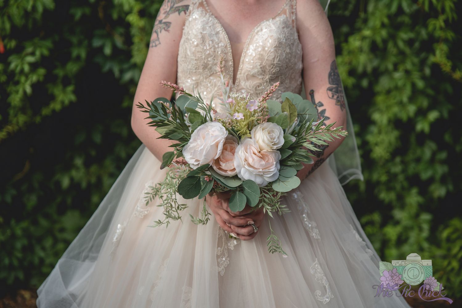Close-up of bridal bouquet featuring pink roses and greenery against a tulle wedding dress.