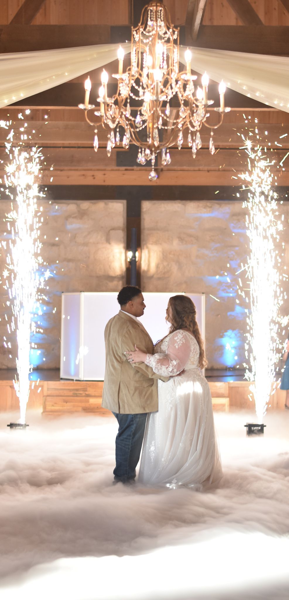 Wedding couple's first dance under a crystal chandelier with fog and sparkler effects.