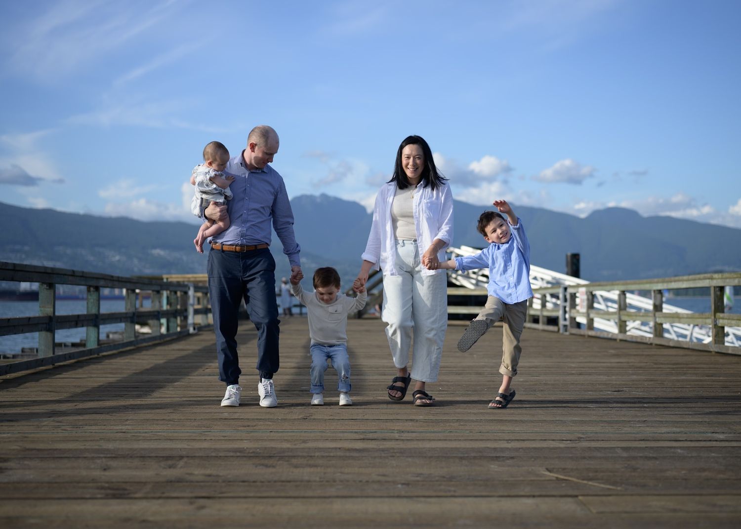 Family of five walking along waterfront pier at Jericho Beach with North Shore mountain views, Vancouver photographer
